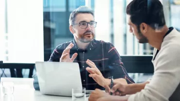 Two men having a discussion at a table with a laptop.