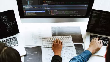 People working on laptops with code on screens, collaborating around a desk.