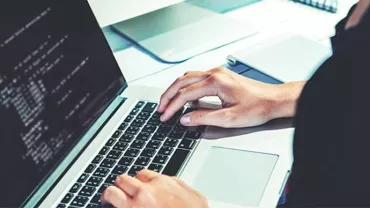 Person typing code on a laptop with a monitor showing code.