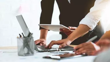 People collaborating at a desk with laptops and tablet.