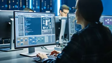 Person analyzing data on multiple computer monitors in a tech office.