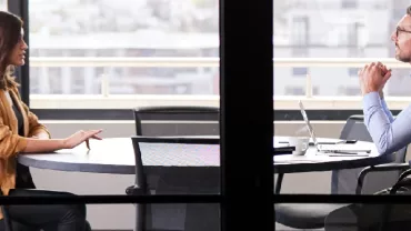 Two professionals having a discussion at a round table in an office setting.