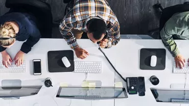 Overhead view of three people working at desks with computers and phones.