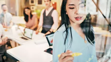 Woman writing on glass board with a marker during a team meeting.