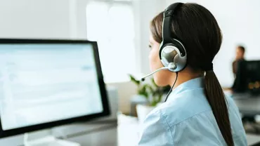 Woman with headset working at a computer in an office setting.