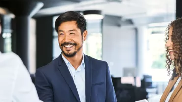 A man in a suit smiling and shaking hands in an office setting.