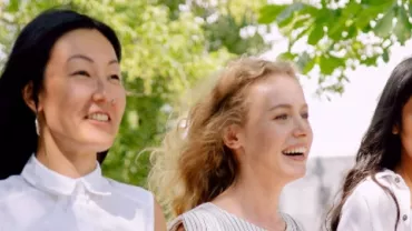 Three women walking outdoors, smiling under trees.