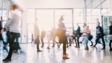 People walking through a busy lobby with glass doors.