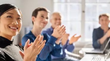 Smiling woman and colleagues clapping in a meeting room.