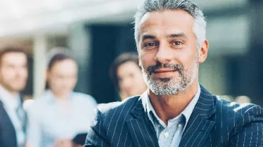 Confident businessman in a suit standing with a blurred office team in the background.