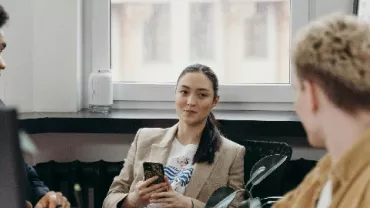 Three people conversing in an office space, one holding a smartphone.