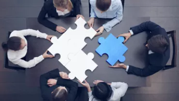 Team of business people assembling large puzzle pieces at a table.