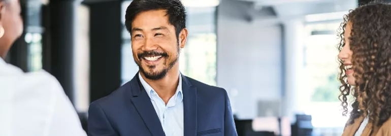 A man in a suit smiling and shaking hands in an office setting.