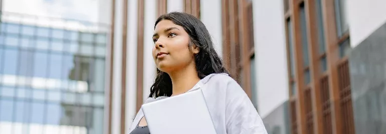 A woman looking pensive outdoors holding a file